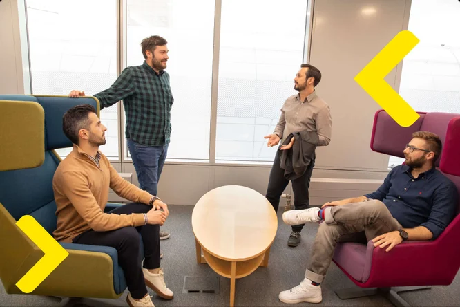 A group of men sitting in office chairs, discussing matters in an office setting.