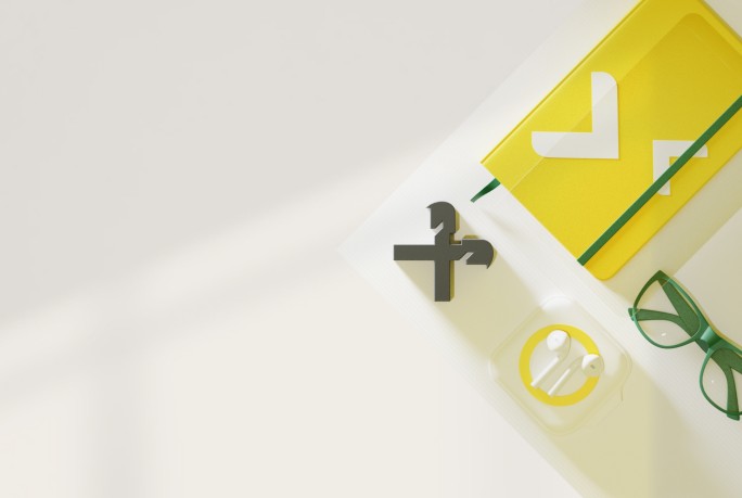 A neatly arranged workspace featuring a yellow notebook, green glasses, wireless earbuds in a charging case, and a decorative symbol. The setup is minimalist and well-lit, ideal for productivity.