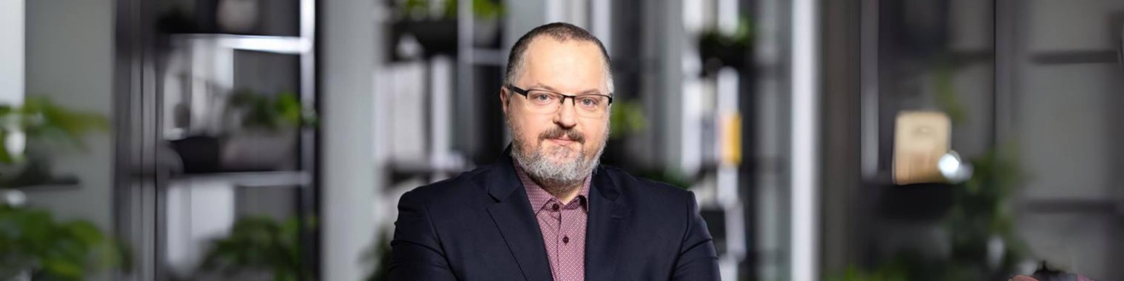 A man with glasses and a beard is seated comfortably in a chair, exuding a relaxed demeanor.
