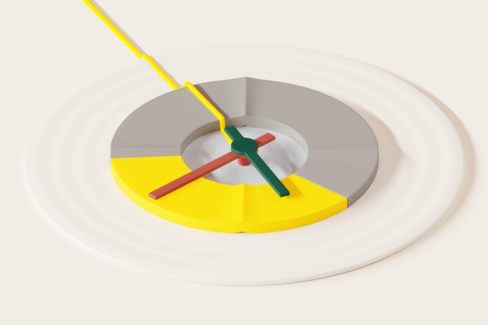 A modern, abstract clock features a circular face divided into yellow and gray segments. The clock hands are colored green, red, and yellow, creating a striking visual contrast. The background is a clean, off-white surface, emphasizing the minimalist and geometric design.