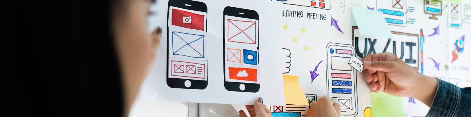 Designers working on UX/UI design for mobile apps, creating user-centric interfaces on a whiteboard.