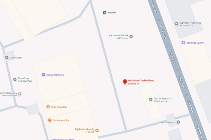The digital map shows the location of Raiffeisen Tech Poland, Building M, in the urban area. Several nearby businesses and checkpoints are marked, including Scena Kotłownia, Sadu Poniedziałek, and Galeria Darkness. The map includes the street name, building outlines, and the visible numerical address of Plac Konstytucji 12. The style is defined and limited, typical of online map interfaces. (opens in a new tab)
